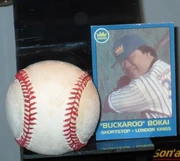 Ein Baseball, der Ball nachdem das Spiel benannt ist. Rechts daneben eine Baseballkarte des Spielers Buck Bokai