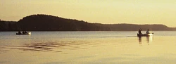 Two canoes paddling into the sunrise on Saganaga Lake, Boundary Waters Canoe Area Wilderness, Minnesota, U.S.A.