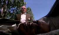 Detective Miles lying inside his car, watched over by an alien bounty hunter disguised as the detective.